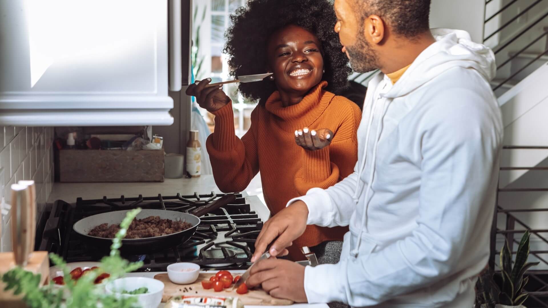 Deux personnes dans une cuisine bien éclairée, souriant en préparant un repas ensemble